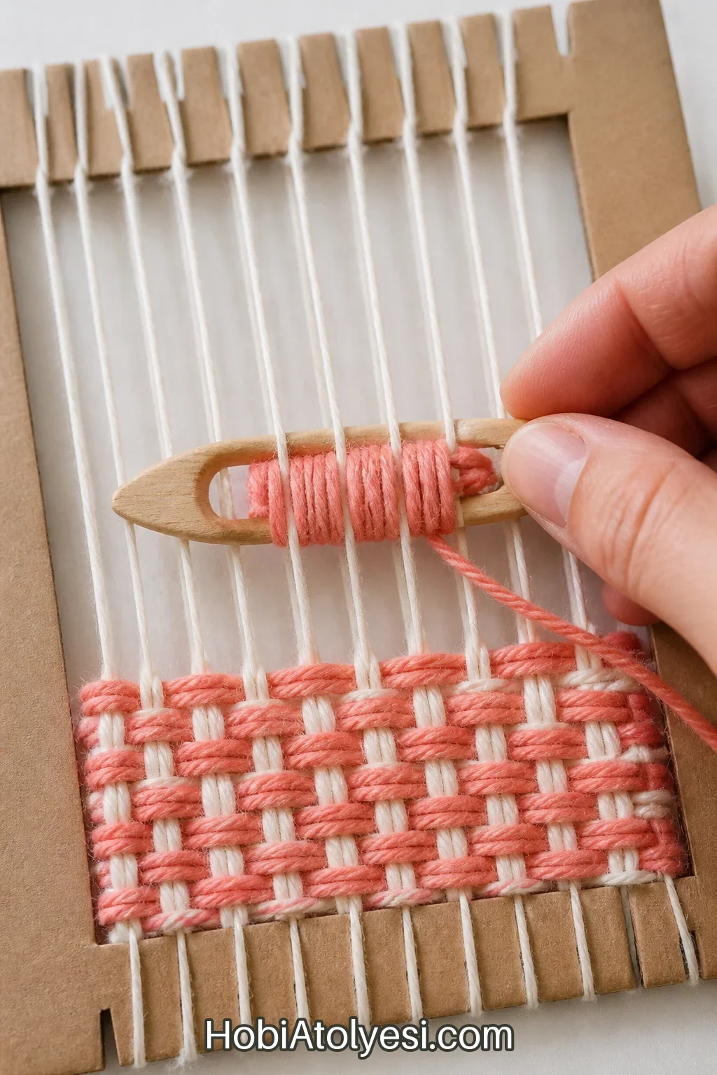 Küçük bir şariğe sarılı pastel ip ile atkı (weft) geçirme gösterimi, şariğin ahşap veya karton